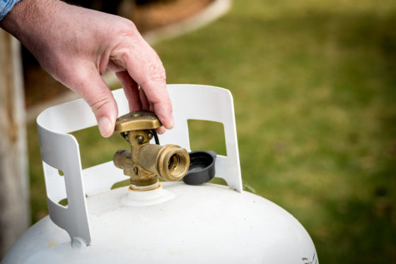 Photo of hand turning valve at top of portable propane tank