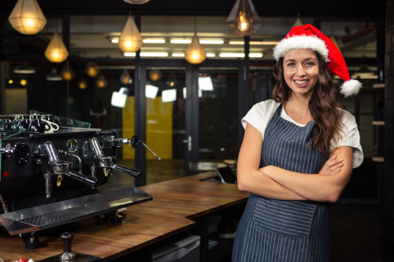 Photo of a barista wearing a santa hat and standing beside a coffee machine