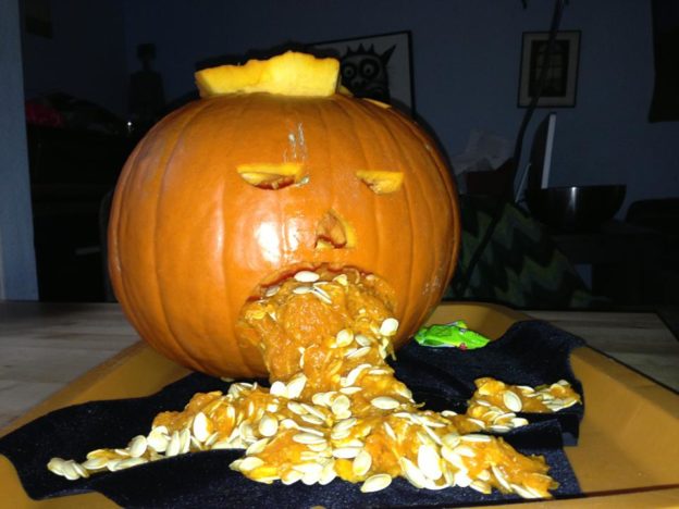 Photo of a Halloween jack-o-lantern with pumpkin seeds coming out of its mouth, looking like vomit