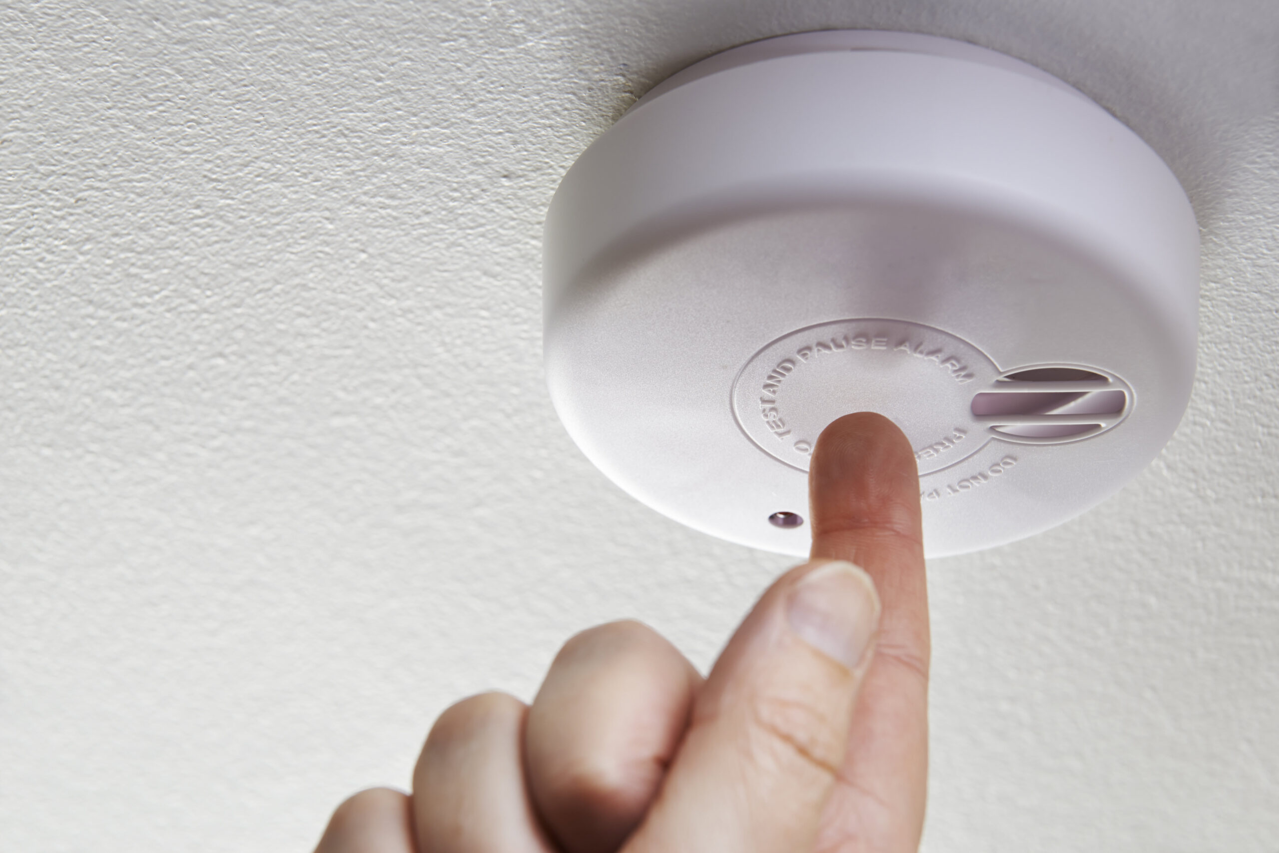 Photo of a hand testing a domestic smoke alarm