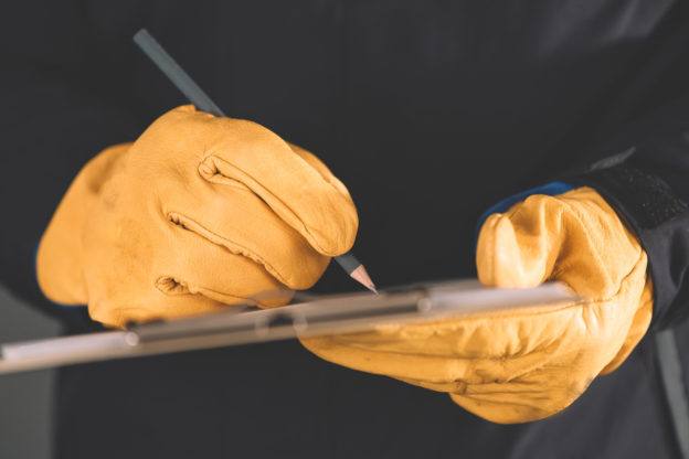 Photo of hands in work gloves, making notes on a clipboard