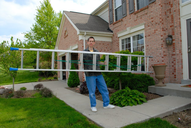 Photo of man carrying extension ladder in front of house
