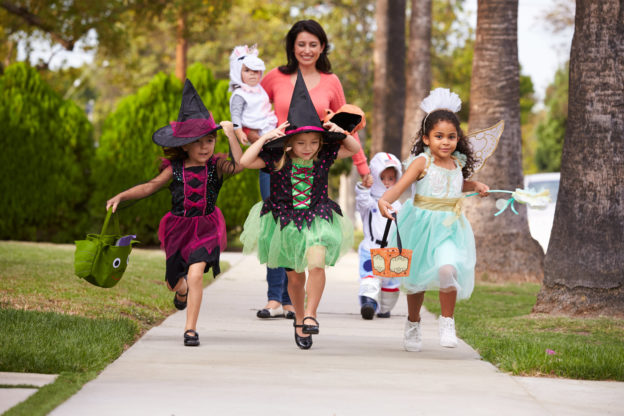 Photo of woman taking children in Halloween costumes along a sidewalk
