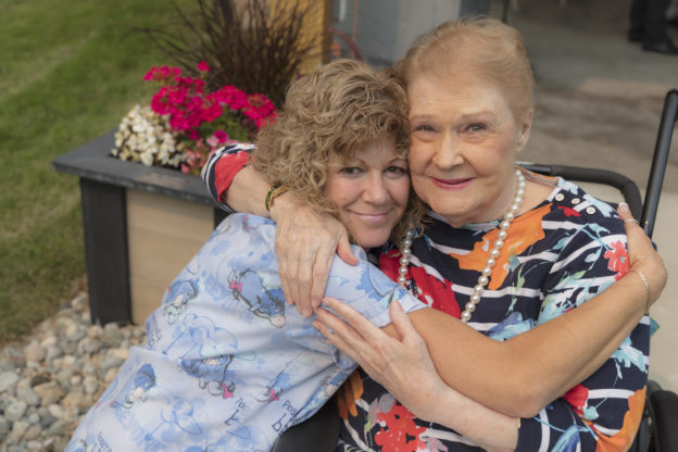 Photo of a care aide and a client in a wheelchair hugging