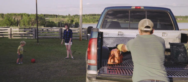 Photo of rancher putting tools in pickup truck with family in background