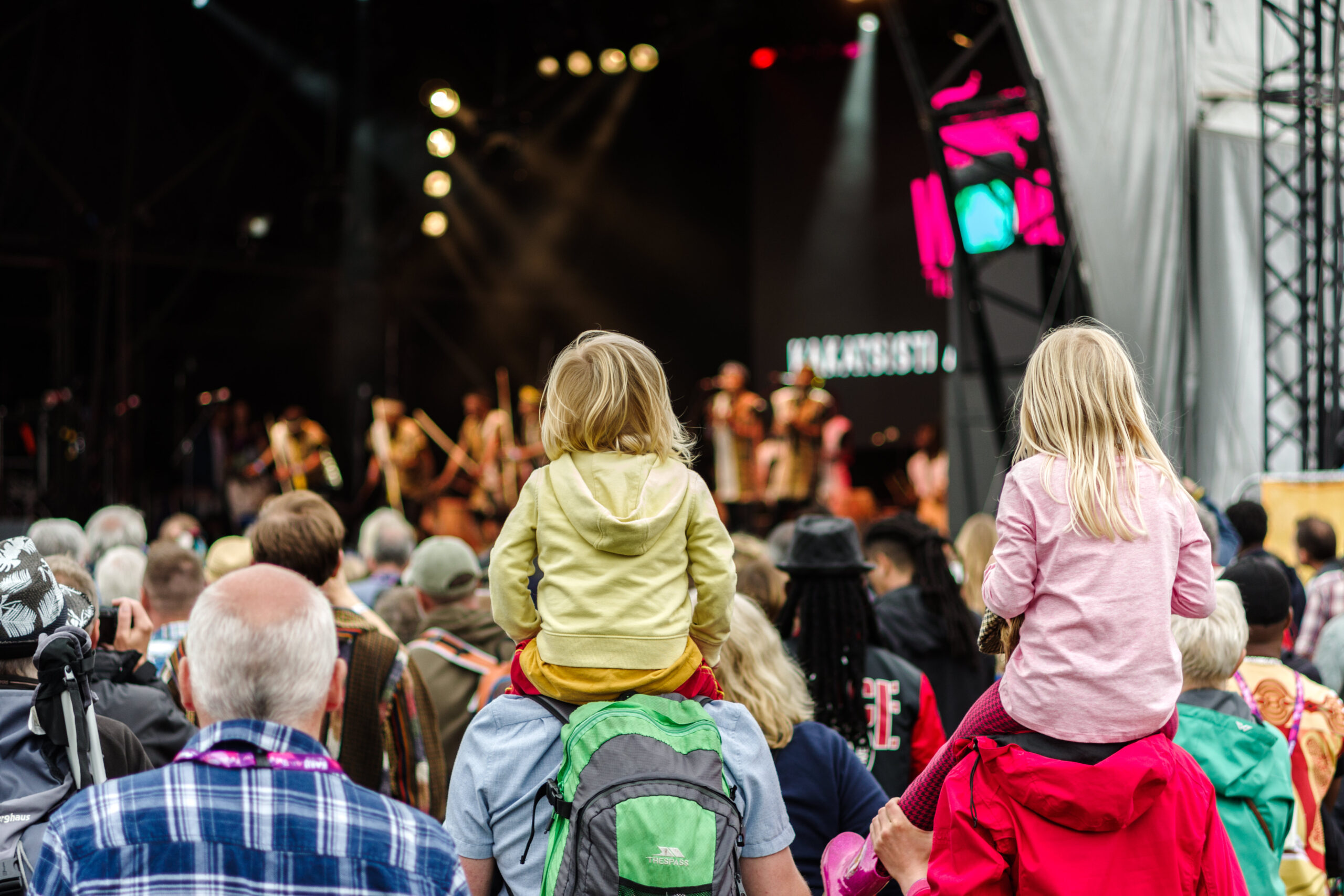 Photo of children on shoulders of adults in audience of concert on big stage