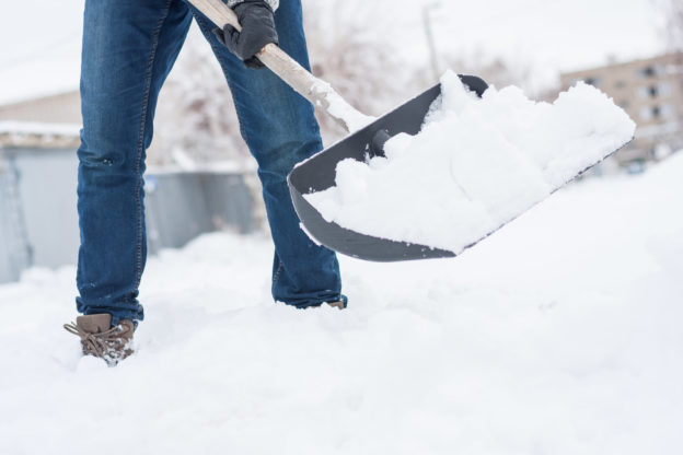 Photo of person in jeans in deep snow with a shovel full of snow