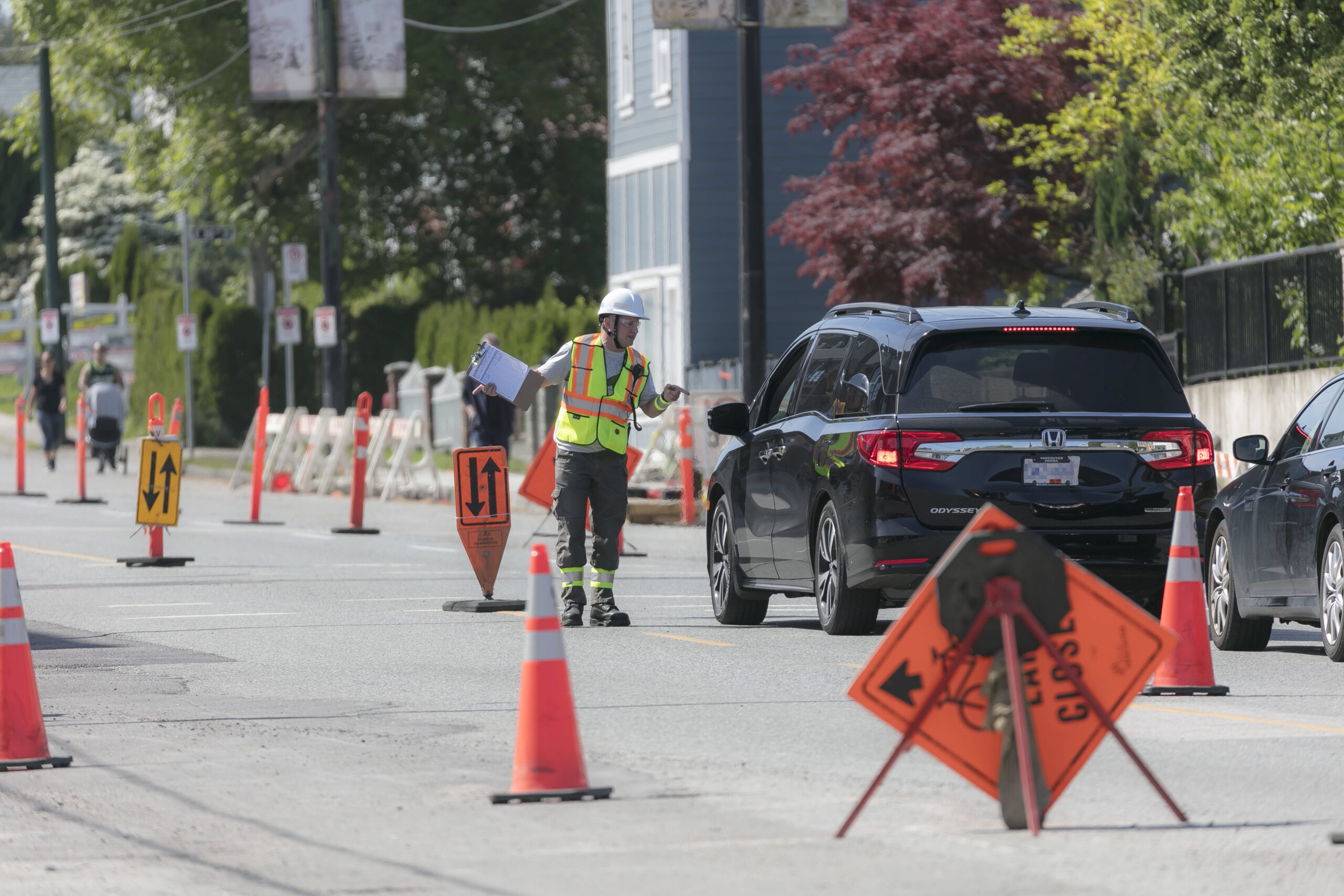 Photo of traffic control person speaking to driver of black SUV, amid traffic cones and signs