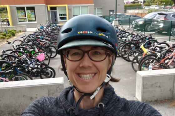 Photo of Lisa Corriveau wearing bike helmet, in front of rows of bikes at her kids' school