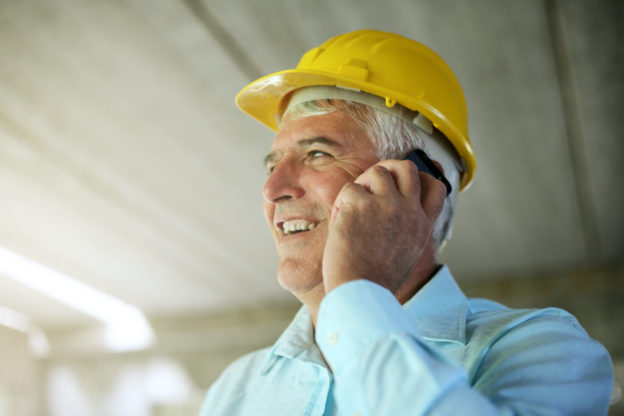 Photo of man wearing a yellow hardhat, talking on cellphone