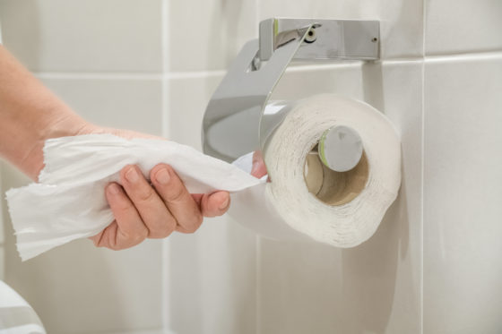 Photo of a hand pulling toilet paper from a roll on a wall next to an unseen toilet