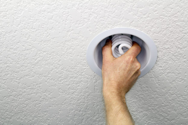 Photo of a hand installing spiral compact fluorescent lightbulb in a recessed white ceiling fixture