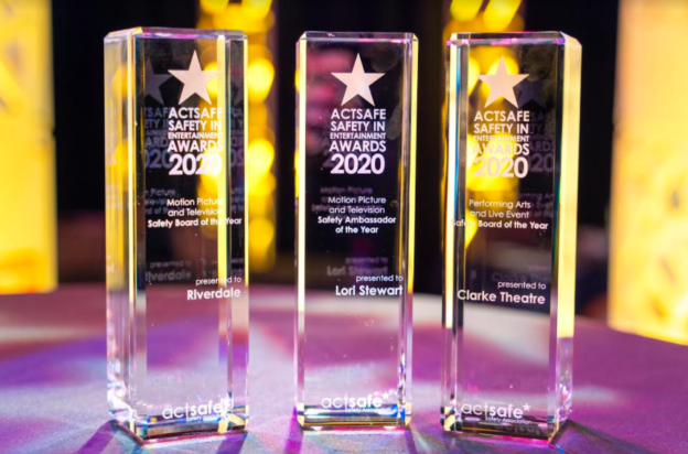Photo of three Actsafe Safety in Entertainment awards, glass pillars against a backdrop of yellow and purple lights