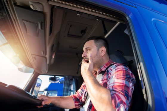 Photo of fatigued truck driver yawning in the driver's seat.