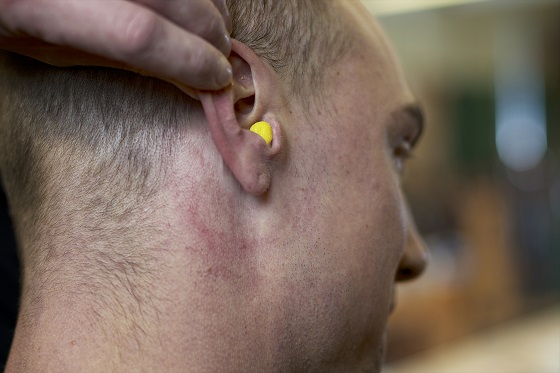 Photo of man pulling back right ear with hearing protection inserted