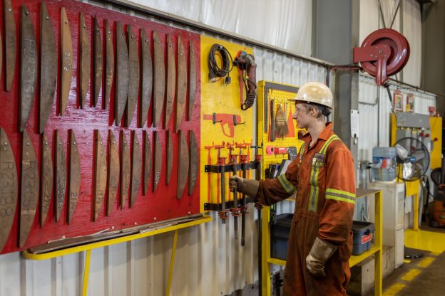 Photo of worker taking a tool from an organized wall of tools in manufacturing facility.