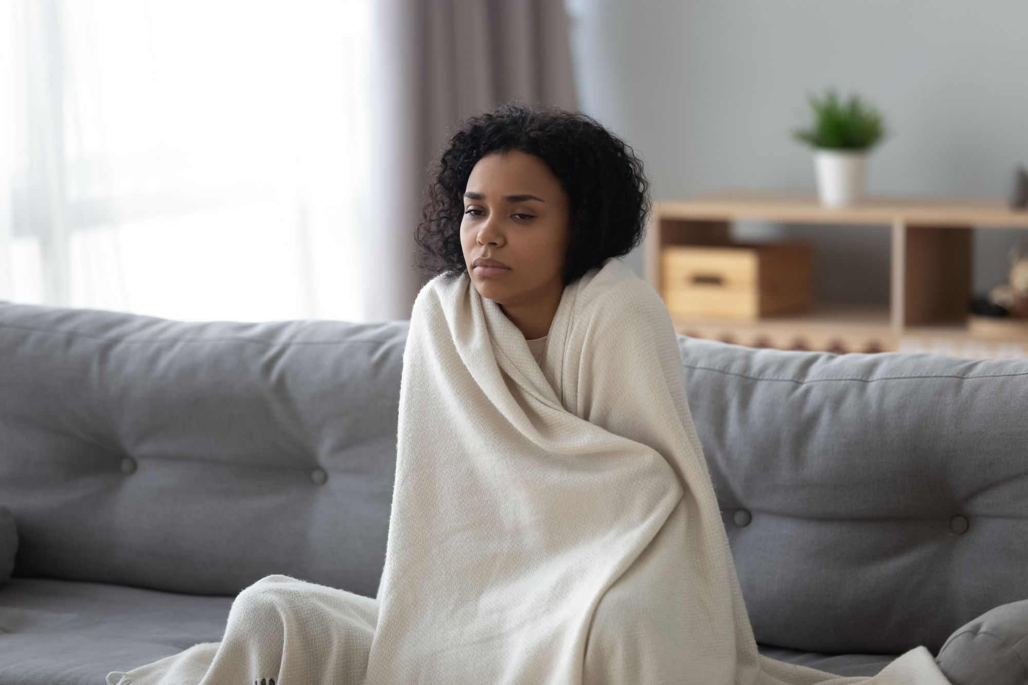 Photo of sick woman sitting on sofa while covered in a blanket.