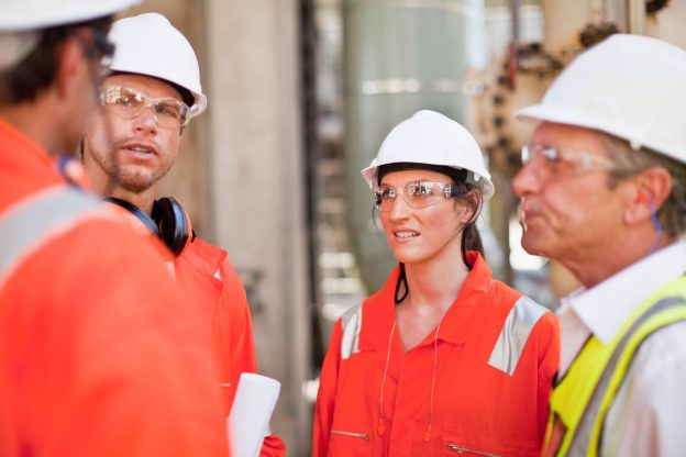 Photo of a group of workers wearing hard hats and safety glasses, standing for a safety meeting