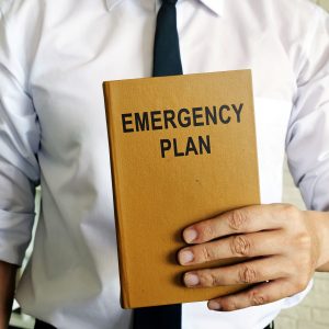 Photo of a person in a shirt and tie, holding an evacuation and emergency plan book in front of them.