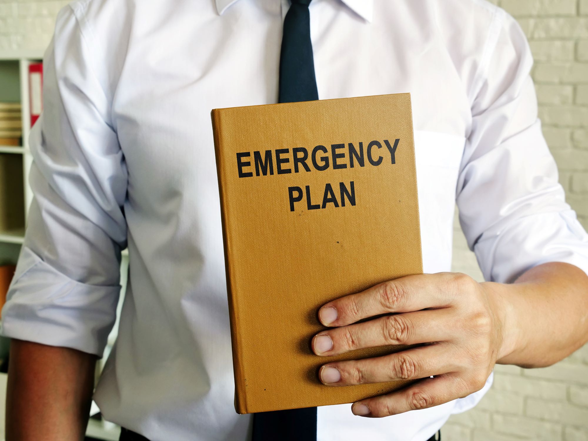Photo of a person in a shirt and tie, holding an emergency plan book in front of them.