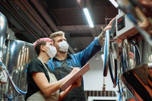 Photo of young worker and employer looking at a control panel while working at a brewery. 