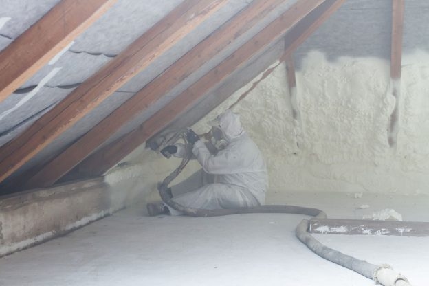 Photo of technician spraying foam insulation using plural component gun for polyurethane foam, inside