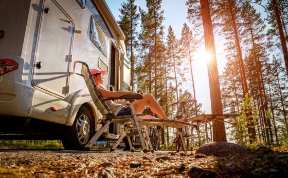 Photo of Person reclined in lounge chair beside camper van near trees