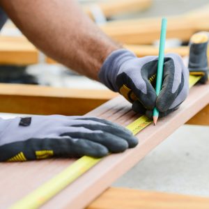 Photo of close up detail of flood restoration worker's hands working with a measuring tape and pencil in wood plank