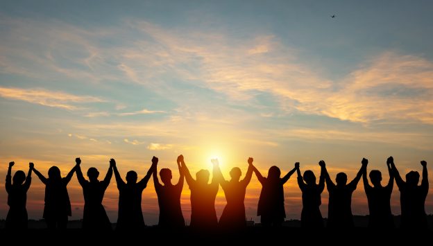 Photo of a silhouette of a group business team making high hands over head in a sunset sky