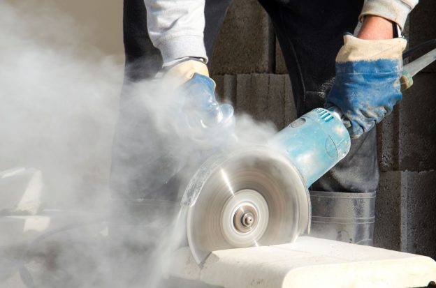 Photo of a circular saw cutting into cement making dust and possible silica exposure.