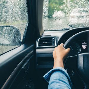 Photo of closeup of driver's hands on steering wheel driving on a rainy day