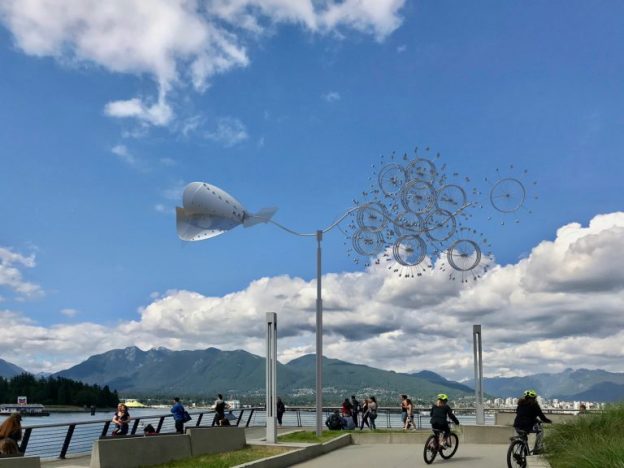 Photo of asbestos memorial mobile installed outside on the waterfront of Vancouver with people riding by it on bicycles