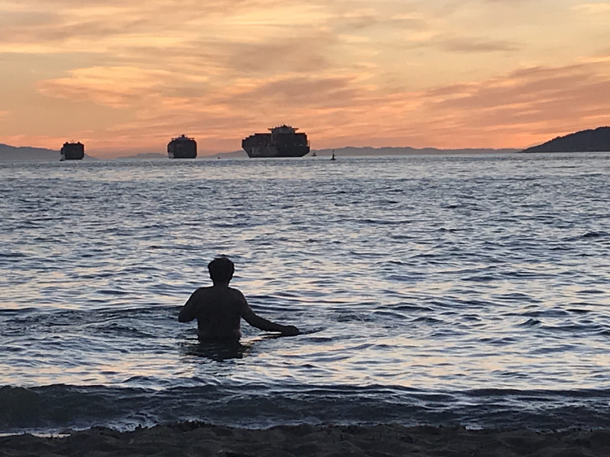 Photo of a person walking into the water at a beach in summer at sunset.