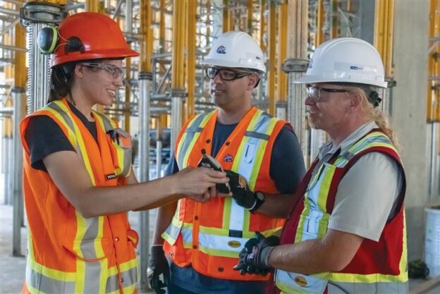 Photo of two men and a woman in PPE talking at a construction site.