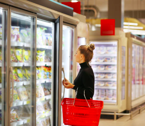 Person in grocery store with shopping basket, looking at food in a freezer