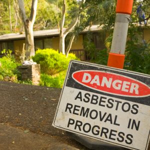 Photo of a sign in front of an older home that says Danger asbestos removal in progress