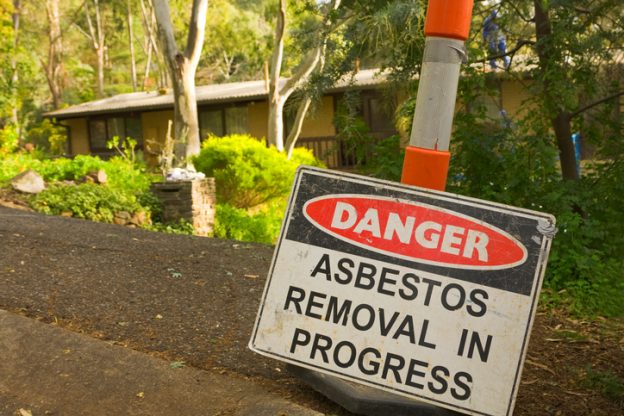 Photo of a sign in front of an older home that says Danger asbestos removal in progress
