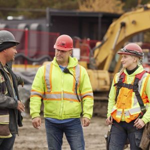 Photo of two males and one female talking at a construction site.