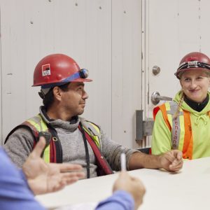 Photo of three individuals in PPE sitting at a table during a safety meeting.