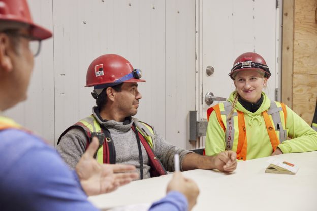Photo of three individuals in PPE sitting at a table during a safety meeting.