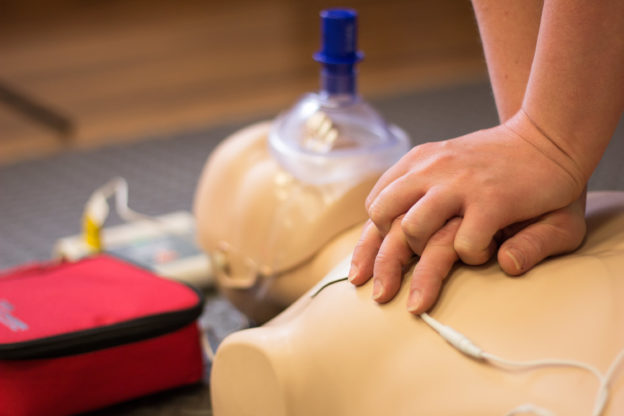 Photo of hands on chest of CPR maniken as person practices chest compressions